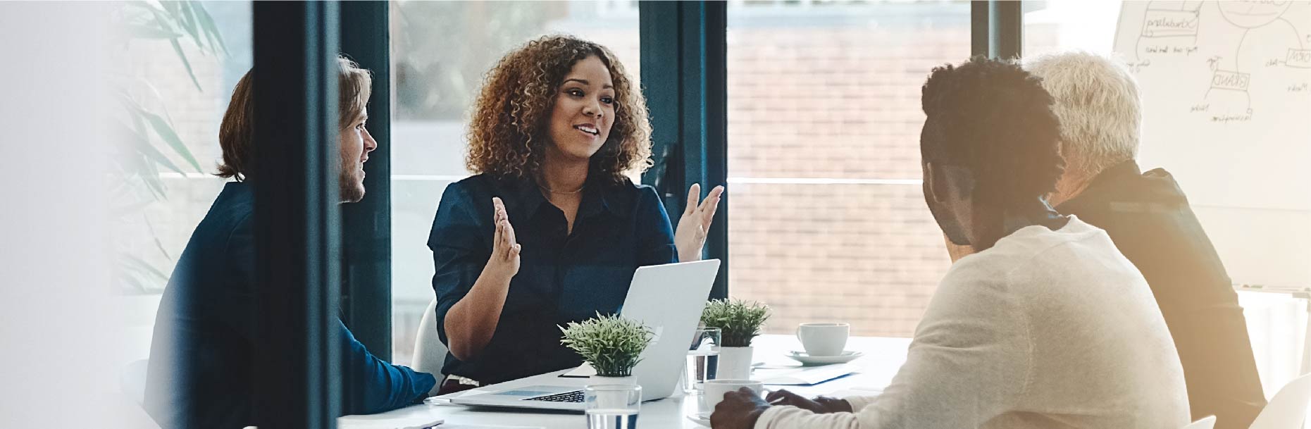 four people in a meeting with a laptop and white board